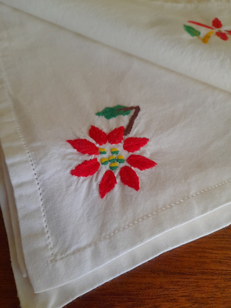 Op de afbeelding: Witte linnen servet met een geborduurde kerstster bloem in rood, groen en geel.
