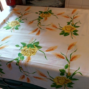 K&ouml;nnte beinhalten: Wei&szlig;e Tischdecke mit einem Muster aus gelben Rosen und Weizen. Die Tischdecke liegt auf einer dunkelgrauen Kommode mit zwei Schubladen.