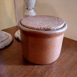 May include: A brown ceramic jar with a cork lid. The jar is sitting on a wooden surface.