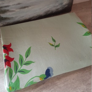 May include: A light green fabric with a floral pattern. The flowers are red, blue, and yellow. The fabric has a textured surface.