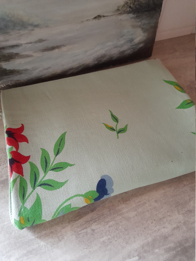 May include: A light green fabric with a floral pattern. The flowers are red, blue, and yellow. The fabric has a textured surface.