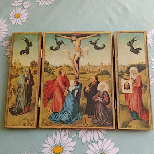 Pode incluir: Um tríptico que retrata a crucificação de Jesus Cristo. O painel central mostra Cristo na cruz, rodeado por figuras em vestes coloridas. Os painéis laterais apresentam cenas e figuras religiosas adicionais, tudo dentro de molduras douradas ornamentadas.