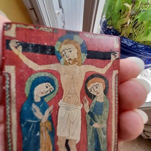 May include: A vintage, hand-painted wooden panel depicting a religious scene. The central figure is Jesus Christ on the cross, with Mary and another woman flanking him. The figures are painted in a stylized, medieval style with vibrant colors.
