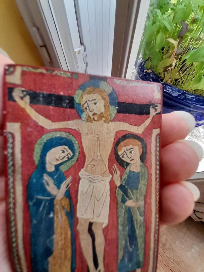 May include: A vintage, hand-painted wooden panel depicting a religious scene. The central figure is Jesus Christ on the cross, with Mary and another woman flanking him. The figures are painted in a stylized, medieval style with vibrant colors.