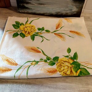 K&ouml;nnte beinhalten: Wei&szlig;e Tischdecke mit einem Design aus gelben Rosen und Weizen. Die Tischdecke hat einen wei&szlig;en Hintergrund mit gr&uuml;nen Bl&auml;ttern und gelben Weizen&auml;hren. Die Rosen sind gelb mit einer wei&szlig;en Mitte.