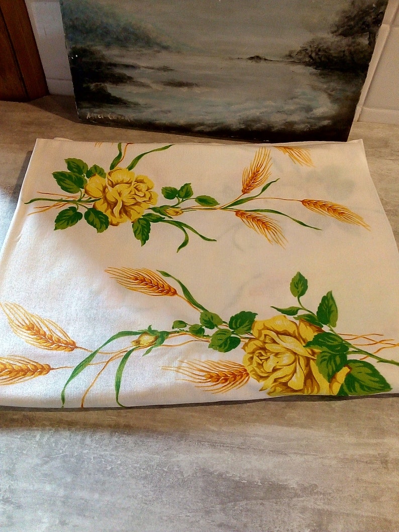 K&ouml;nnte beinhalten: Wei&szlig;e Tischdecke mit einem Design aus gelben Rosen und Weizen. Die Tischdecke hat einen wei&szlig;en Hintergrund mit gr&uuml;nen Bl&auml;ttern und gelben Weizen&auml;hren. Die Rosen sind gelb mit einer wei&szlig;en Mitte.