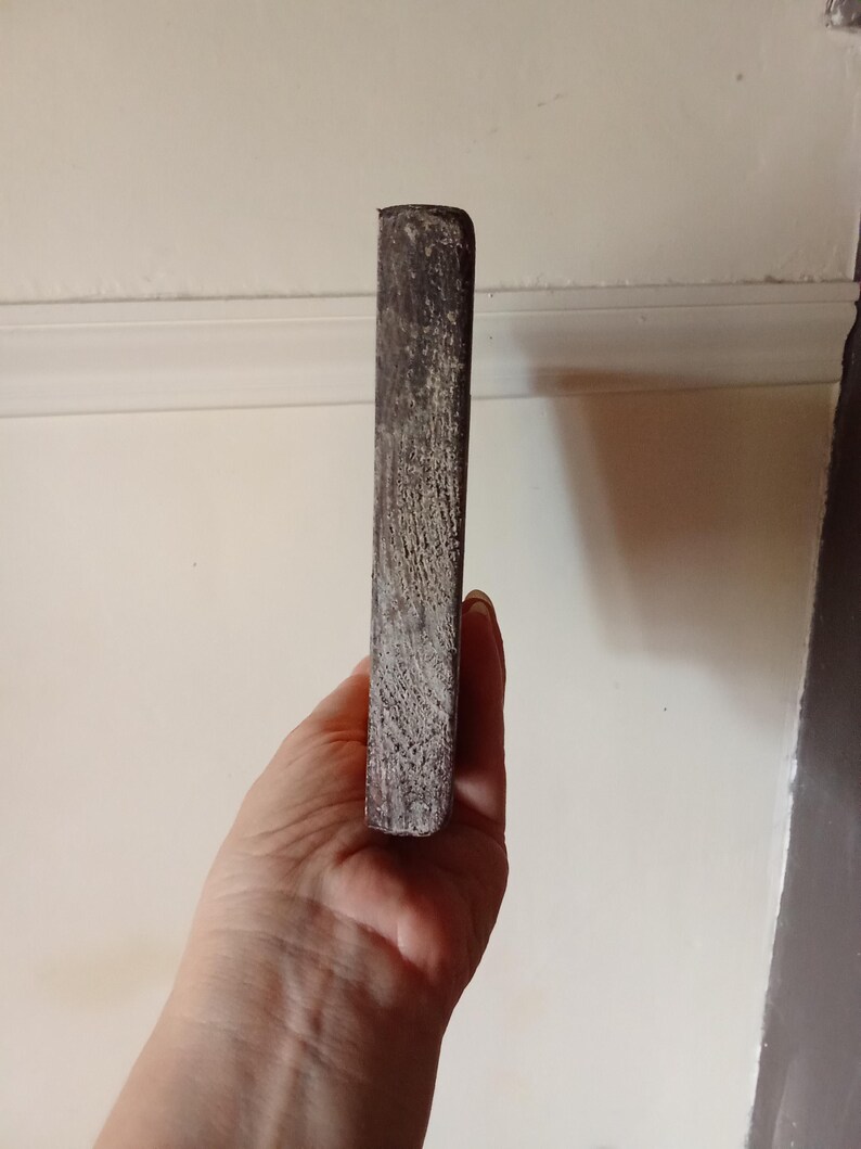May include: A rectangular block of dark, weathered wood with a rough, textured surface. The object has a deep brown color with visible grain patterns and worn edges, showing a natural, aged appearance throughout its solid, elongated form.