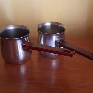 Peut inclure: Deux cafetières en argent avec des poignées rouges. Les cafetières sont sur une surface en bois.