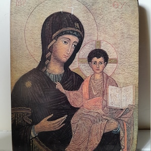 Può includere: Un'icona religiosa in stile vintage che raffigura la Vergine Maria che tiene in braccio un giovane Gesù. L'icona è dipinta su un pannello di legno con sfondo dorato e presenta un'aureola intorno alle teste di Maria e Gesù. Il testo sull'icona recita "Εγω ειμι το φως" che si traduce in "Io sono la luce".