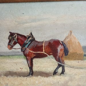 May include: Oil painting of a brown horse harnessed for work in a field. The horse stands in a field with a haystack in the background. The painting is framed in a dark wood frame.