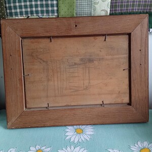 May include: Back of a rectangular wooden picture frame. The frame is a medium brown color and has a simple, classic design. The back is made of a light-colored wood and is secured with small metal staples.