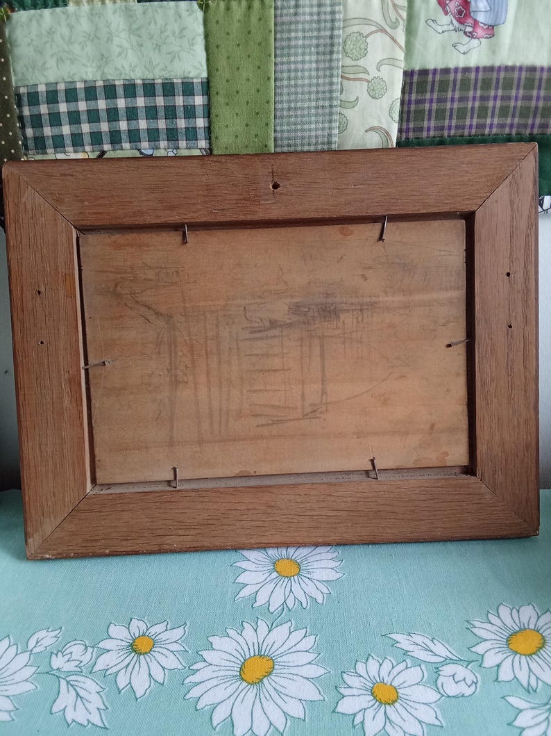 May include: Back of a rectangular wooden picture frame. The frame is a medium brown color and has a simple, classic design. The back is made of a light-colored wood and is secured with small metal staples.
