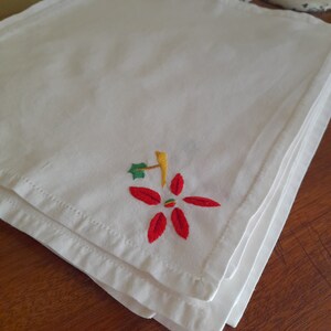 Op de afbeelding: Een stapel witte linnen servetten met een geborduurd rood en groen kerststermotief.