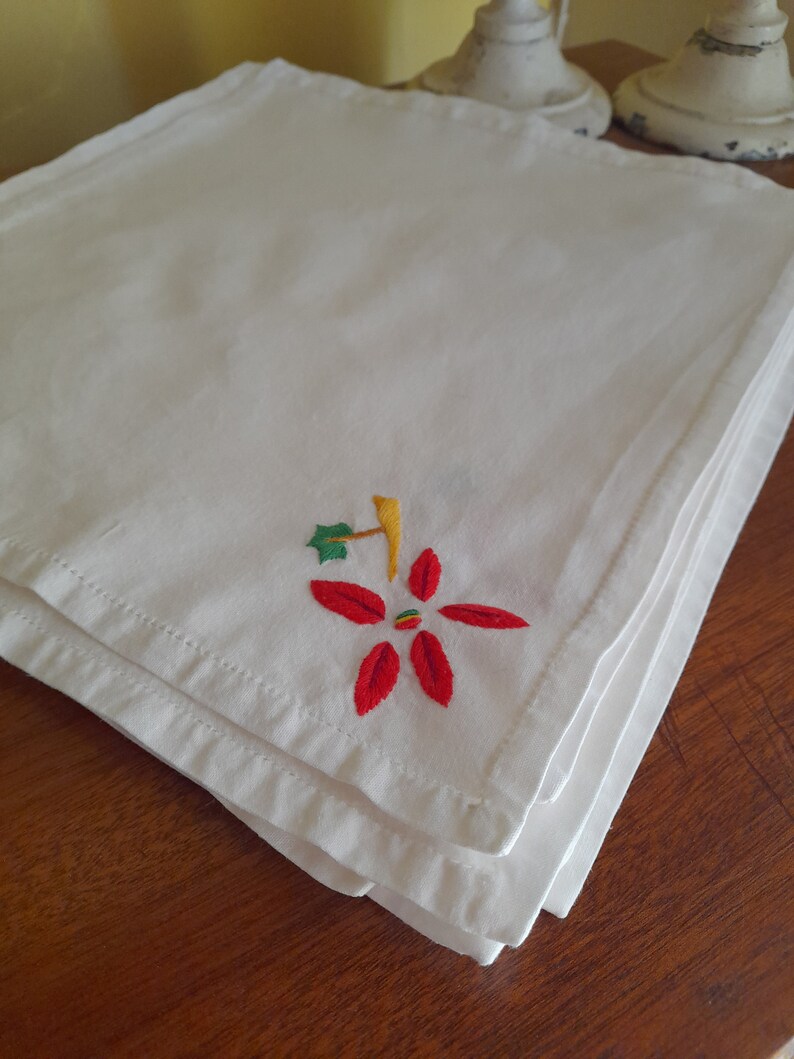 Op de afbeelding: Een stapel witte linnen servetten met een geborduurd rood en groen kerststermotief.