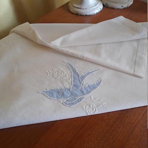 May include: White linen tablecloth with blue embroidered bird and floral design.