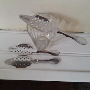 May include: Three silver metal spoons with a perforated design and the word "Pernod" printed on the handle. The spoons are used for stirring absinthe.
