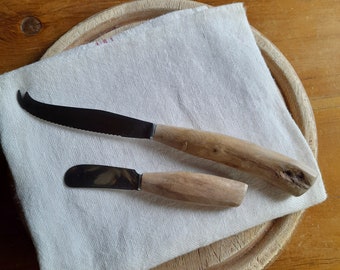 May include: Two wooden handled cheese knives on a white linen napkin on a wooden cutting board.