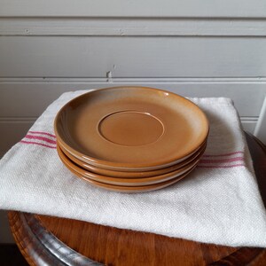 May include: A stack of four brown ceramic saucers. The saucers are stacked on a white linen cloth with red stripes.