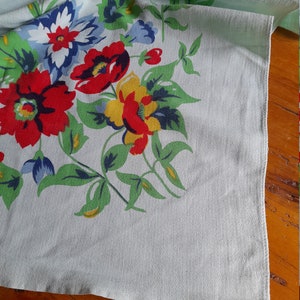 May include: A vintage tablecloth with a floral pattern in shades of red, blue, yellow, and green on a light blue background.