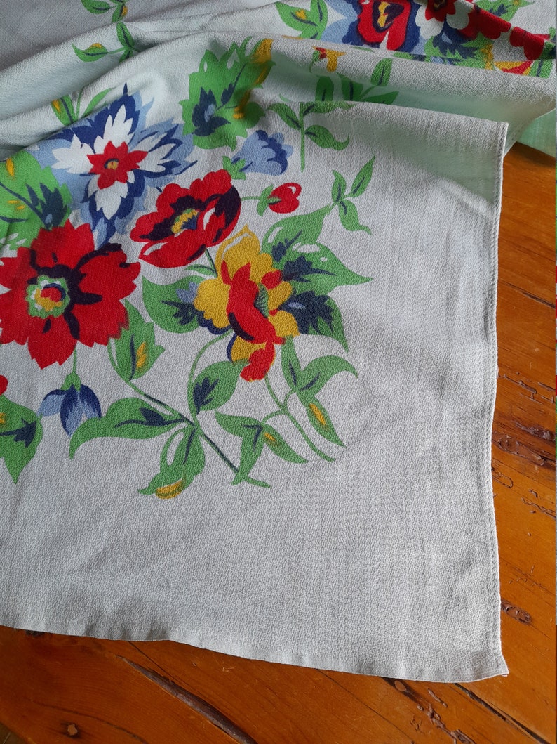 May include: A vintage tablecloth with a floral pattern in shades of red, blue, yellow, and green on a light blue background.
