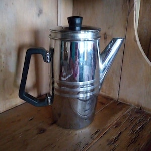 May include: A silver coffee pot with a black handle and lid. The pot has a shiny, reflective surface and a simple design.