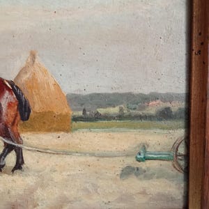 May include: An oil painting in a wooden frame depicts a rural scene. A brown horse pulls a green cart across a field. A haystack and distant trees are visible under a cloudy sky. The painting has a rustic, vintage aesthetic.