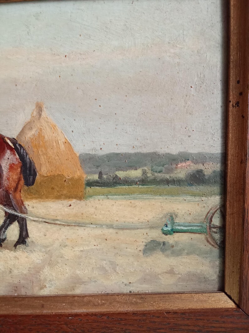 May include: An oil painting in a wooden frame depicts a rural scene. A brown horse pulls a green cart across a field. A haystack and distant trees are visible under a cloudy sky. The painting has a rustic, vintage aesthetic.