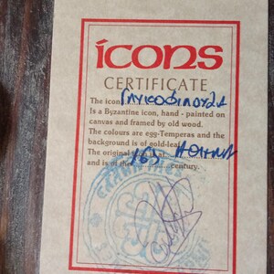 May include: A rectangular certificate of authenticity for a Byzantine icon, printed on light beige paper with a red border. The text reads "icons CERTIFICATE" and includes handwritten blue ink details, a circular blue stamp, and a signature at the bottom.