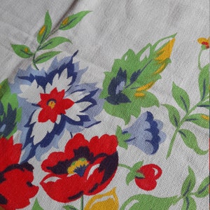 May include: A white tablecloth with a floral pattern. The pattern features red, yellow, blue, and green flowers and leaves.