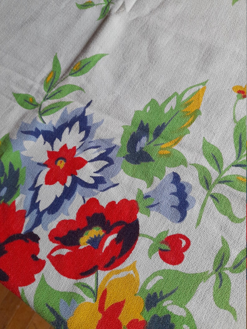 May include: A white tablecloth with a floral pattern. The pattern features red, yellow, blue, and green flowers and leaves.