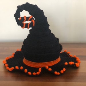 May include: A black witch hat with an orange brim and a curled black top. The hat has a scalloped edge with orange pom-poms.