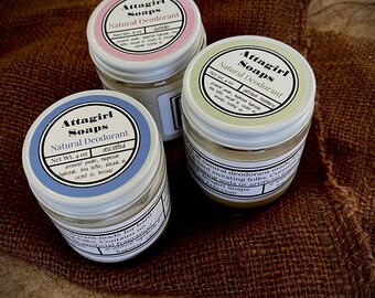 May include: Three jars of Attagirl Soaps natural deodorant, each with a different label color: pink for lavender, green for patchouli rosemary, and blue for unscented. The jars are on a brown burlap surface.