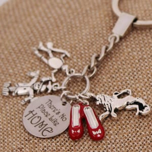 May include: Silver keychain with a charm that says "There's No Place Like Home" and other charms including ruby slippers, a lion, a scarecrow, and a tin man.