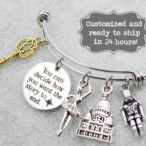 May include: Silver charm bracelet with a key, ballerina, Eiffel Tower, and nutcracker charms. The bracelet has a round charm with the text "You can decide how you want the story to end."