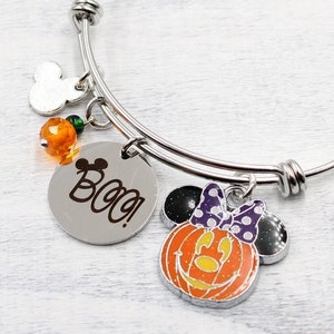 May include: A silver bangle bracelet with charms. The charms include a Mickey Mouse head, orange beads, a round charm with the word "Boo!" and a pumpkin-shaped charm with a Minnie Mouse face.