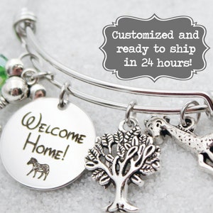 May include: Silver charm bracelet with a round charm that says "Welcome Home!" and a zebra silhouette. The bracelet also has a charm of a tree, a giraffe, a key, and a green crystal.