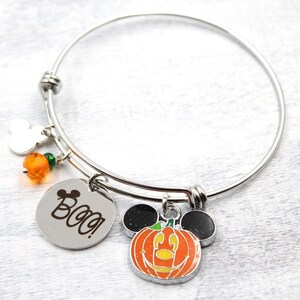 May include: A silver charm bracelet with a pumpkin Mickey Mouse charm, a silver charm with the word "Boo!" engraved on it, and orange and green beads.