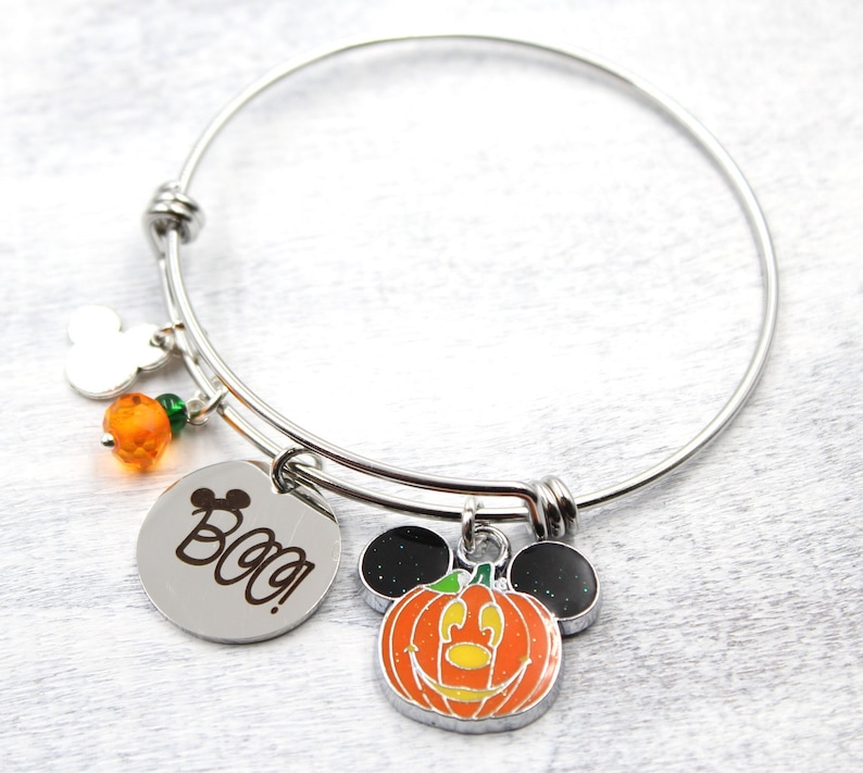 May include: A silver charm bracelet with a pumpkin Mickey Mouse charm, a silver charm with the word "Boo!" engraved on it, and orange and green beads.