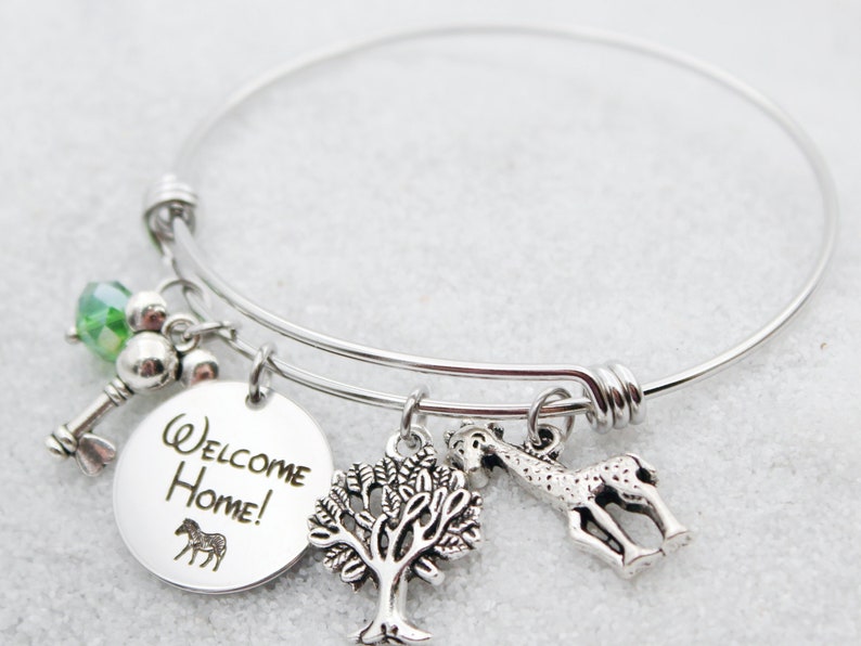 May include: Silver charm bracelet with a round charm that says "Welcome Home!" and features a zebra, a tree charm, a giraffe charm, a key charm, and a green crystal bead.