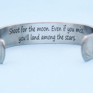 May include: A silver bracelet with an engraved inspirational quote: "Shoot for the moon. Even if you miss, you'll land among the stars."
