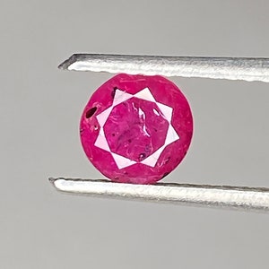 Può includere: Una pietra preziosa di rubino rosa brillante con una taglio a forma di stella, tenuta con delle pinzette.