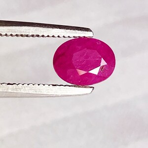 Può includere: Una gemma di rubino ovale di colore rosa vibrante tenuta da una pinzetta.