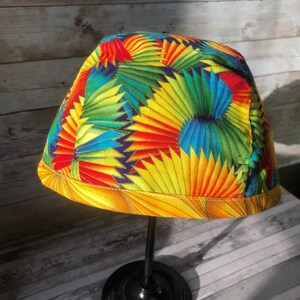 Puede incluir: Un sombrero de tela colorido con un patr&oacute;n geom&eacute;trico amarillo, rojo, azul y verde. El sombrero se muestra en un soporte negro.