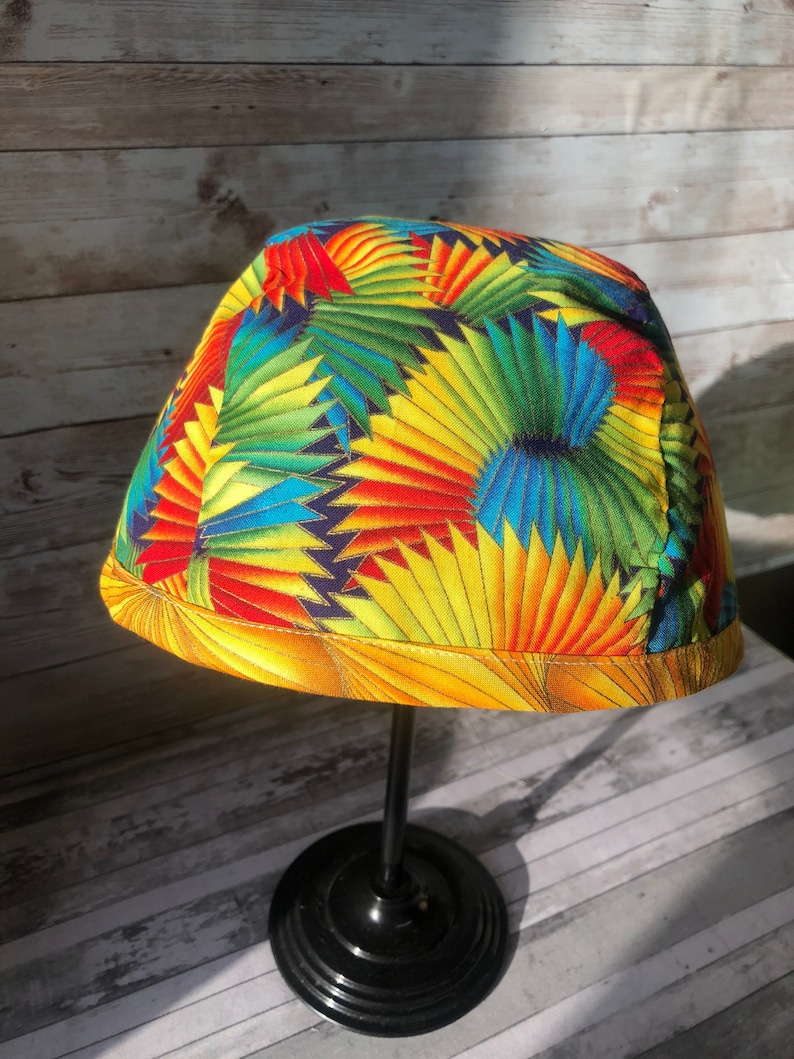 Puede incluir: Un sombrero de tela colorido con un patr&oacute;n geom&eacute;trico amarillo, rojo, azul y verde. El sombrero se muestra en un soporte negro.