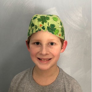 Puede incluir: Una persona joven con un sombrero de papel verde y blanco con un patr&oacute;n de tr&eacute;bol. El sombrero tiene un borde festoneado y est&aacute; decorado con peque&ntilde;os detalles naranjas y verdes.