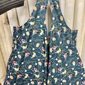 May include: A teal blue tote bag with a white floral pattern and the words "Michigan" and "Wolverine" repeated throughout. The bag has a cutout design on the back.
