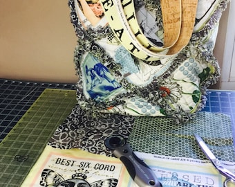 Puede incluir: Primer plano de una bolsa de tela con asa de corcho y una correa amarilla con el texto "TUDES BEE-ATI" impreso en ella. La bolsa está hecha de varias telas con diferentes patrones y colores. La bolsa está sobre una estera de corte verde con un par de tijeras y un cortador rotatorio.