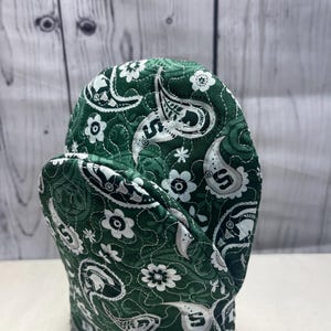 Peut inclure: Manique de cuisine matelassée verte et blanche avec un motif paisley et un logo blanc.