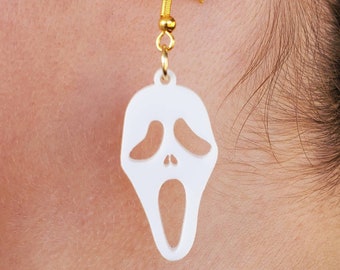 May include: White plastic earrings shaped like the Ghostface mask from the Scream movie franchise. The earrings have gold hooks.