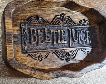 May include: A wooden tray with the words "BEETLEJUICE" carved into the center. The tray has a dark brown finish with a decorative border. The tray is rectangular with rounded edges and a shallow depth.